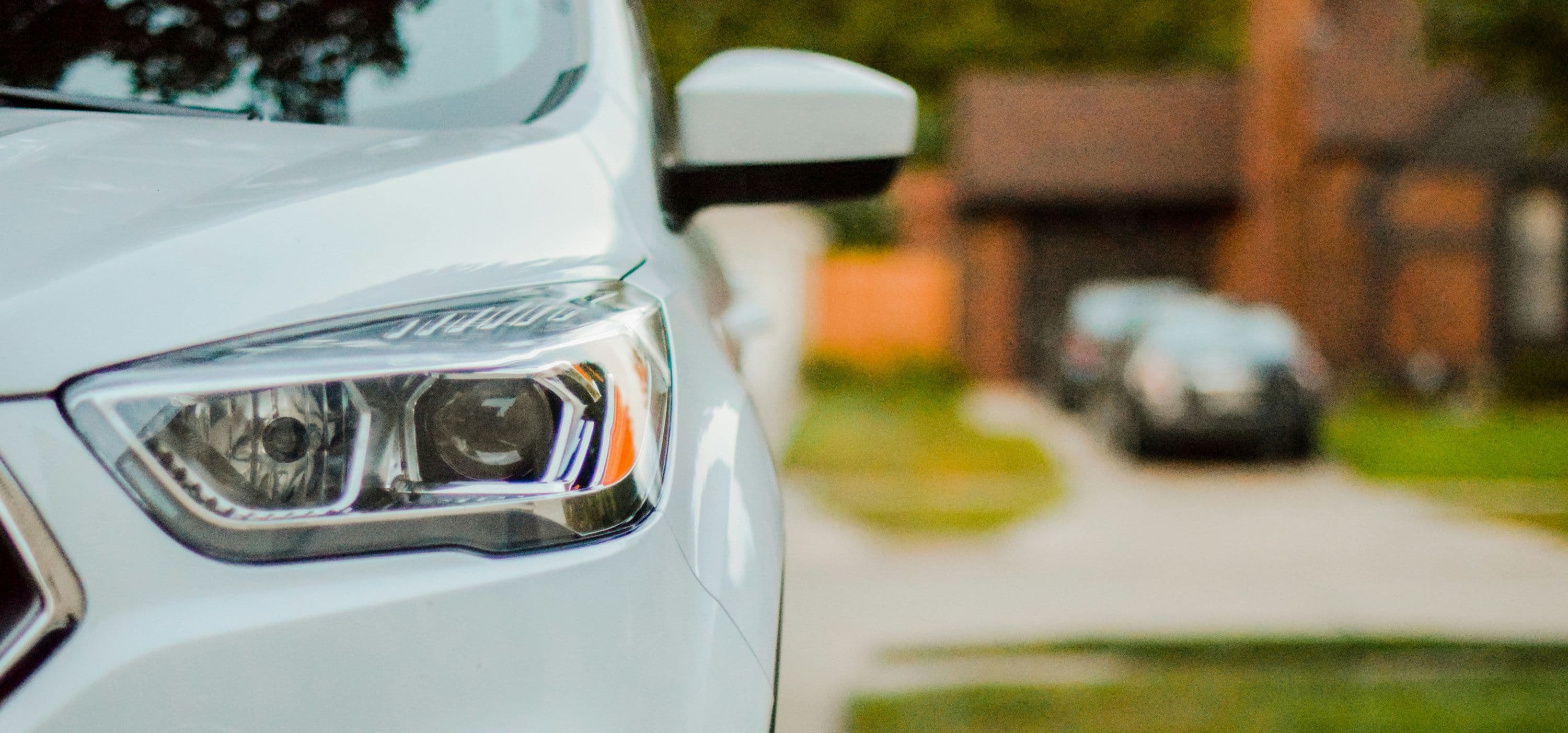 Gros plan sur le phare avant gauche d’un SUV blanc garé dans une allée résidentielle.