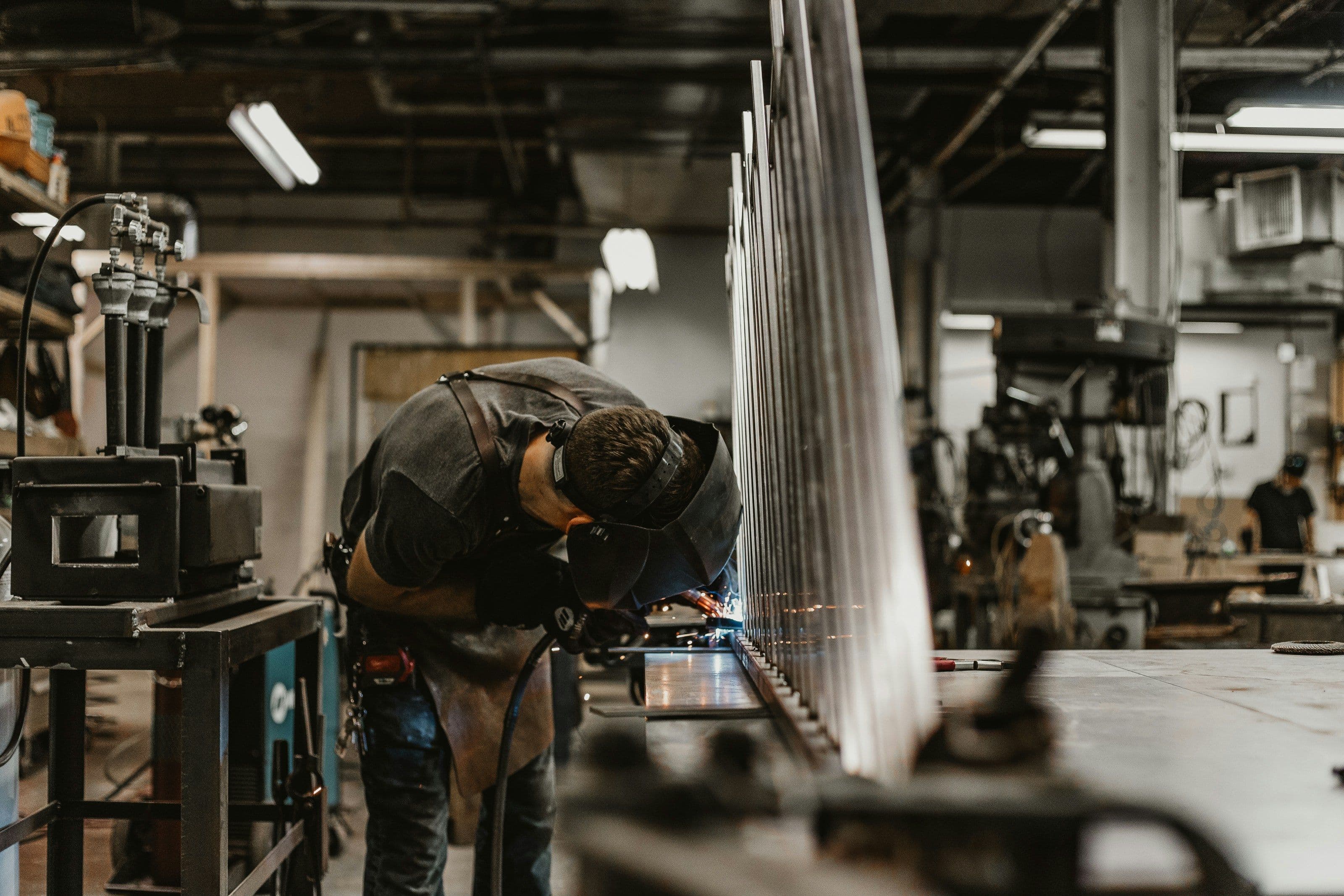 Ouvrier portant un masque de protection en train de souder des pièces métalliques dans un atelier industriel.