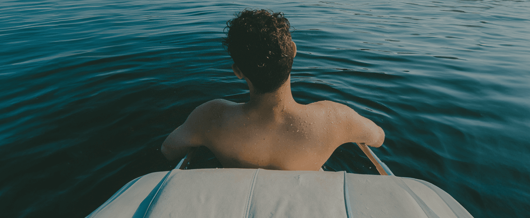 Homme torse nu vu de dos descendant d’un bateau dans une eau sombre et calme.