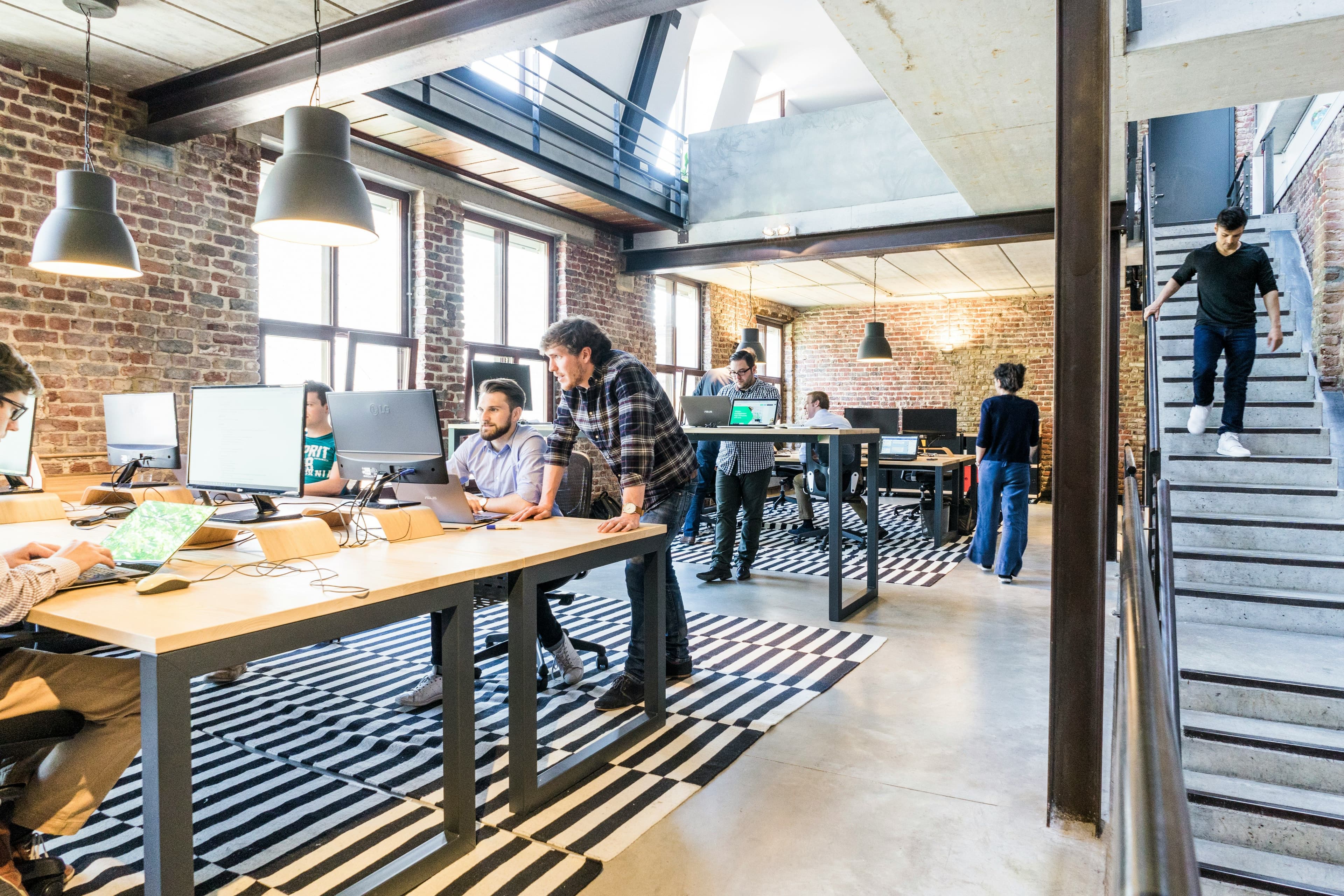 Espace de coworking lumineux au style industriel avec briques apparentes, où plusieurs personnes travaillent sur ordinateurs ou discutent.