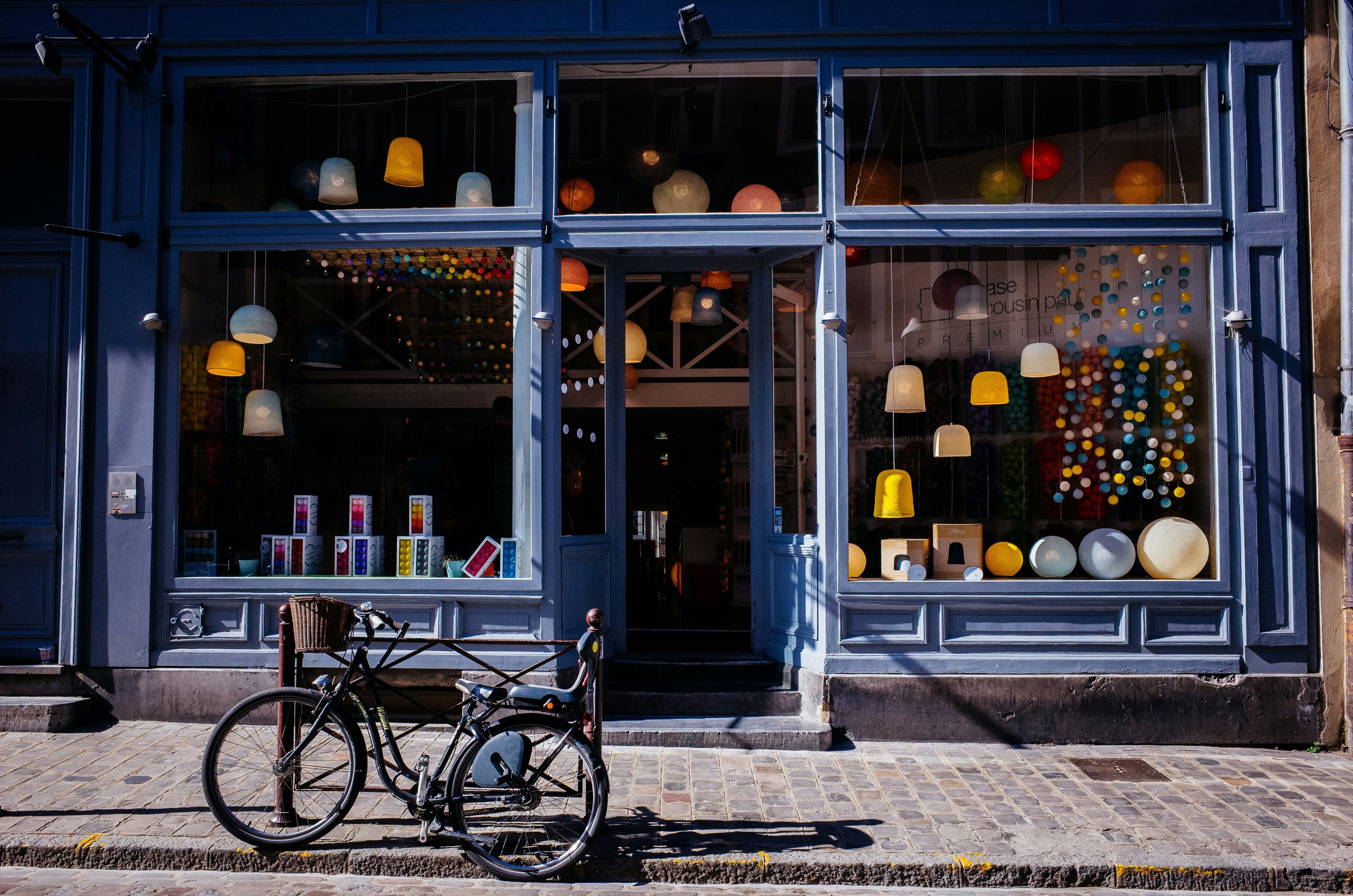 Vitrine d’un magasin de luminaires colorés avec une façade bleue, un vélo noir attaché au poteau devant.