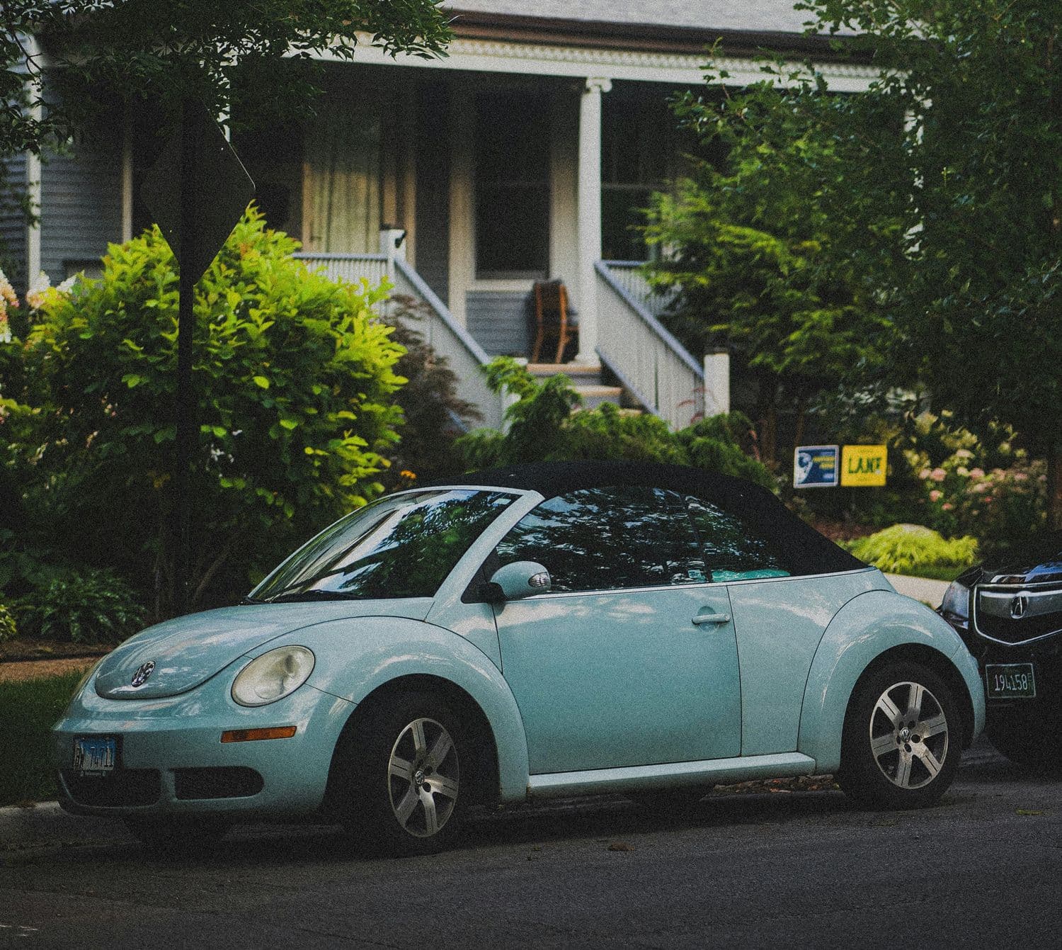 Coccinelle cabriolet bleu clair stationnée devant une maison avec un porche et un jardin arboré.